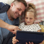 father and daughter lying on floor using digital tablet